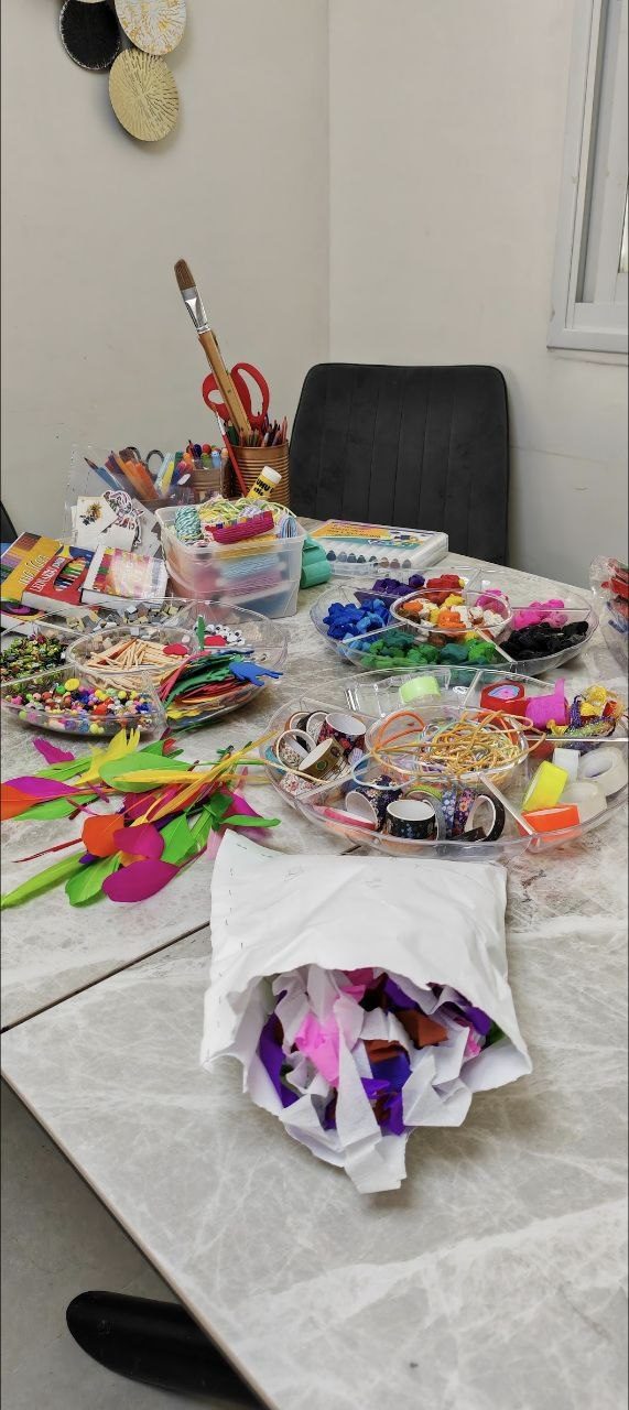 Studio table set with feathers, beads, tape, and tissue paper